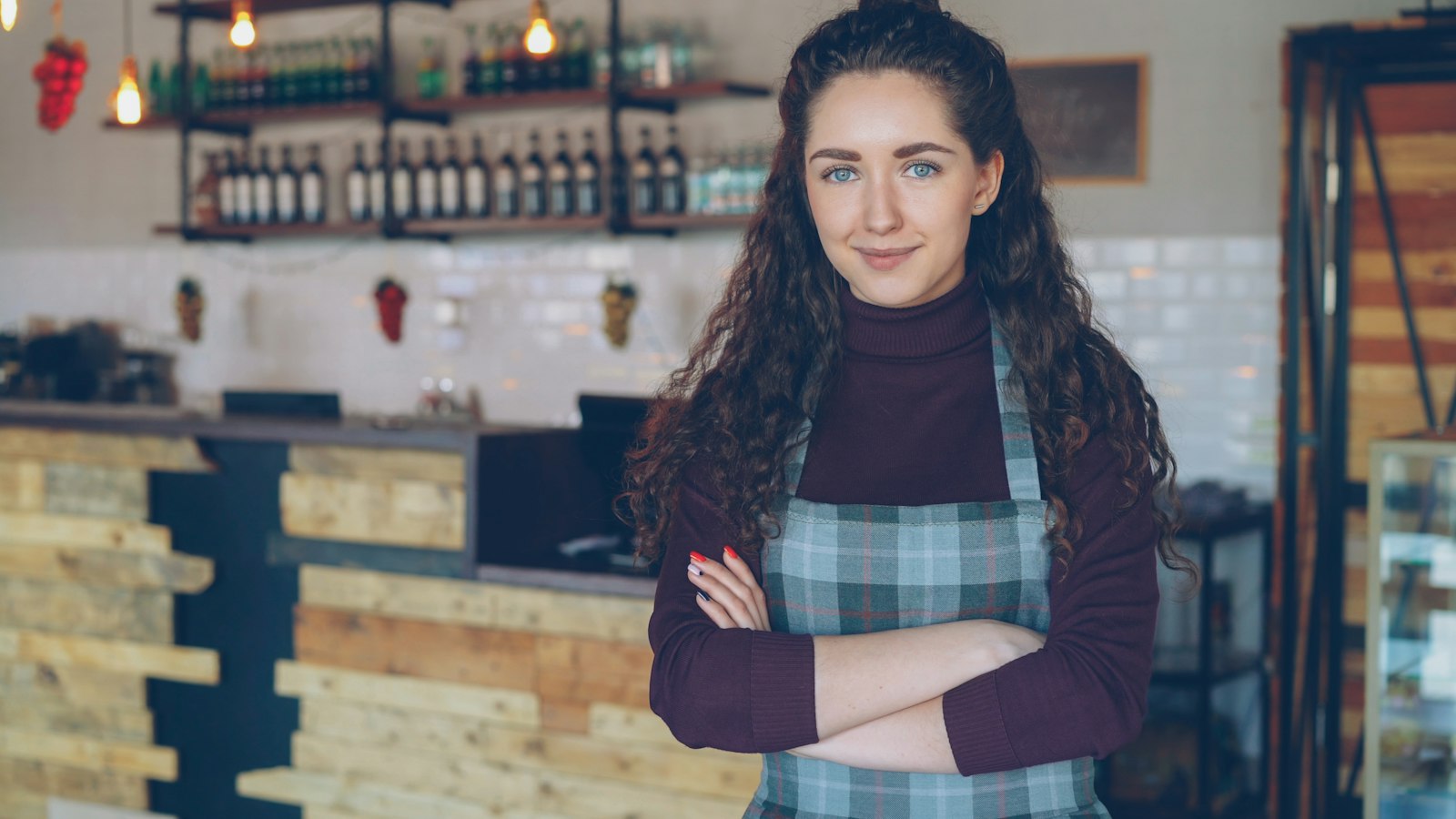 A local business owner standing confidently at the counter of her shop, arms crossed and smiling.